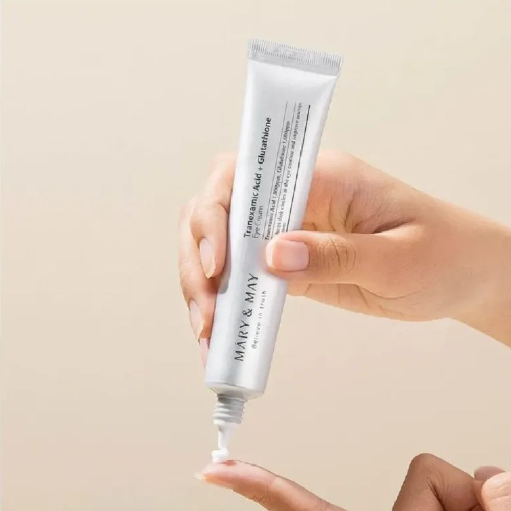 Una mano tiene un tubetto di crema contorno occhi Mary & May, una piccola quantità viene applicata su un dito.
