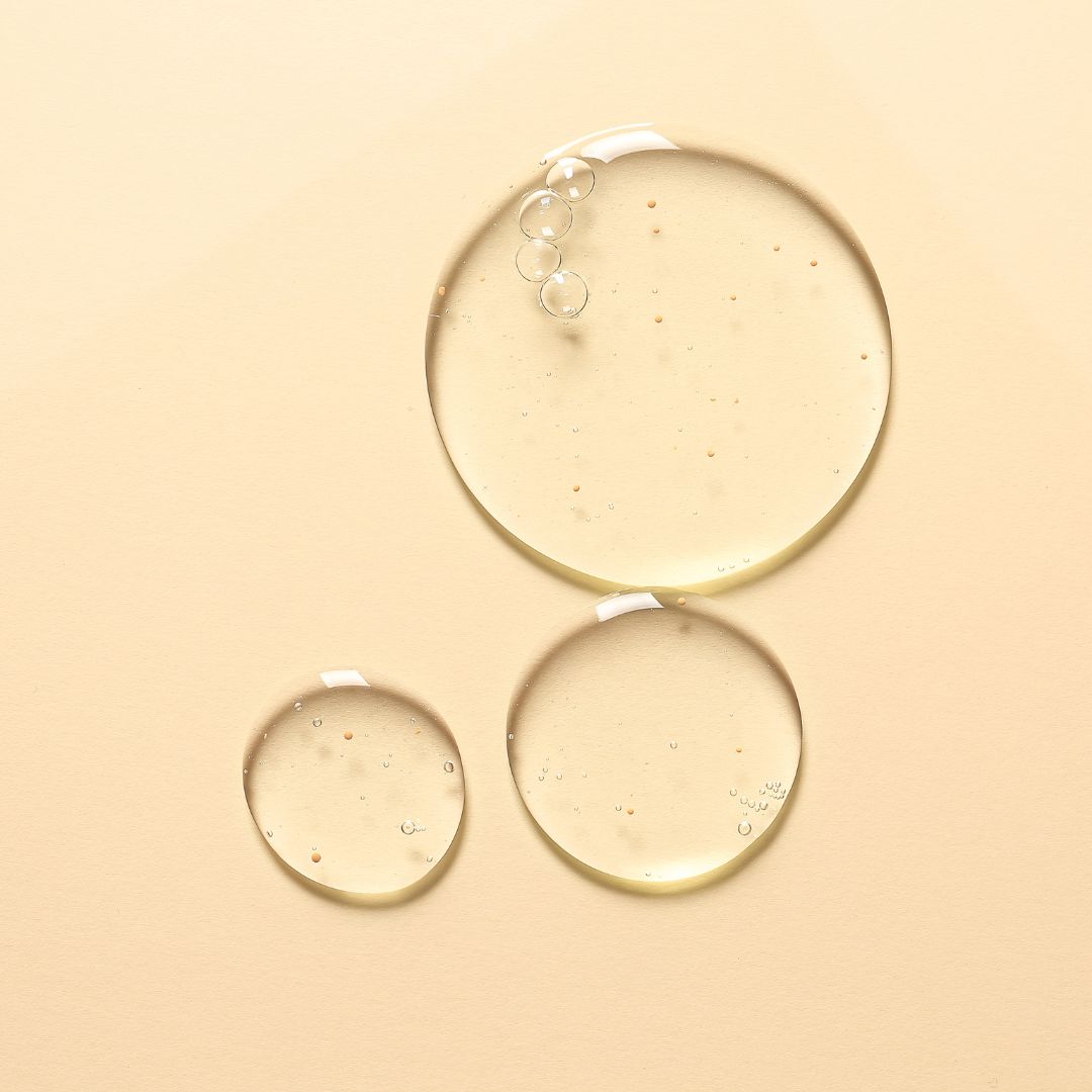 Tre gocce rotonde trasparenti e alcune bolle su sfondo beige.