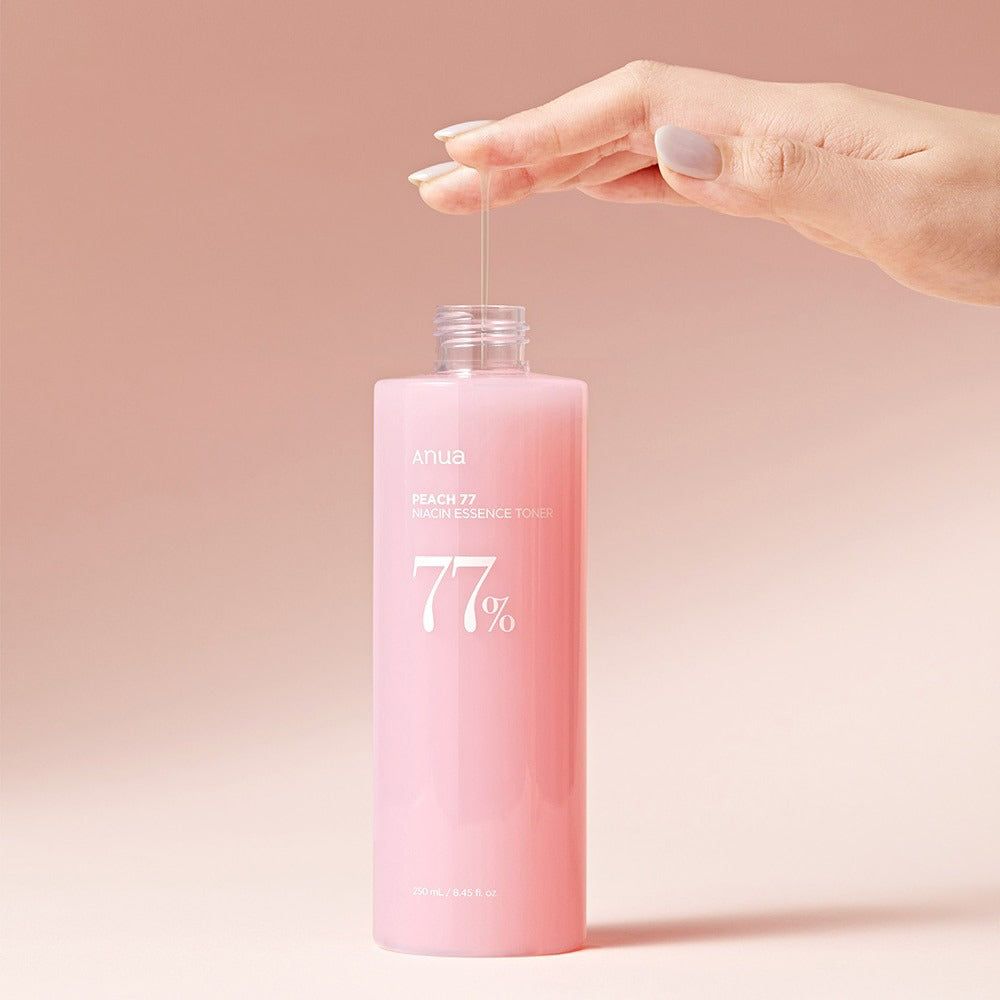 Flacone rosa con tappo bianco. Mano che tiene liquido. Scritta: Peach 77 Niacin Essence Toner. 77% in bianco.