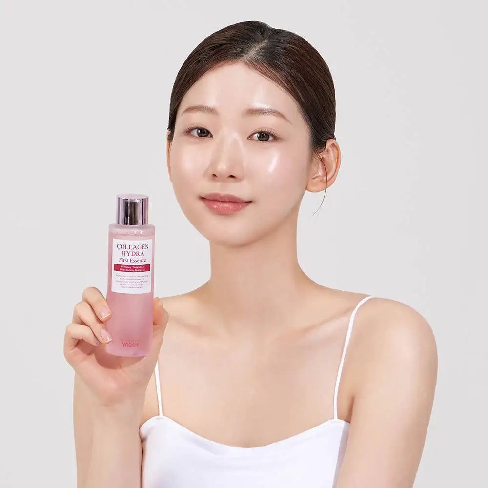 Donna tiene in mano un flacone di liquido rosa. Scritta: Collagen Hydra First Essence. La donna indossa un top bianco.