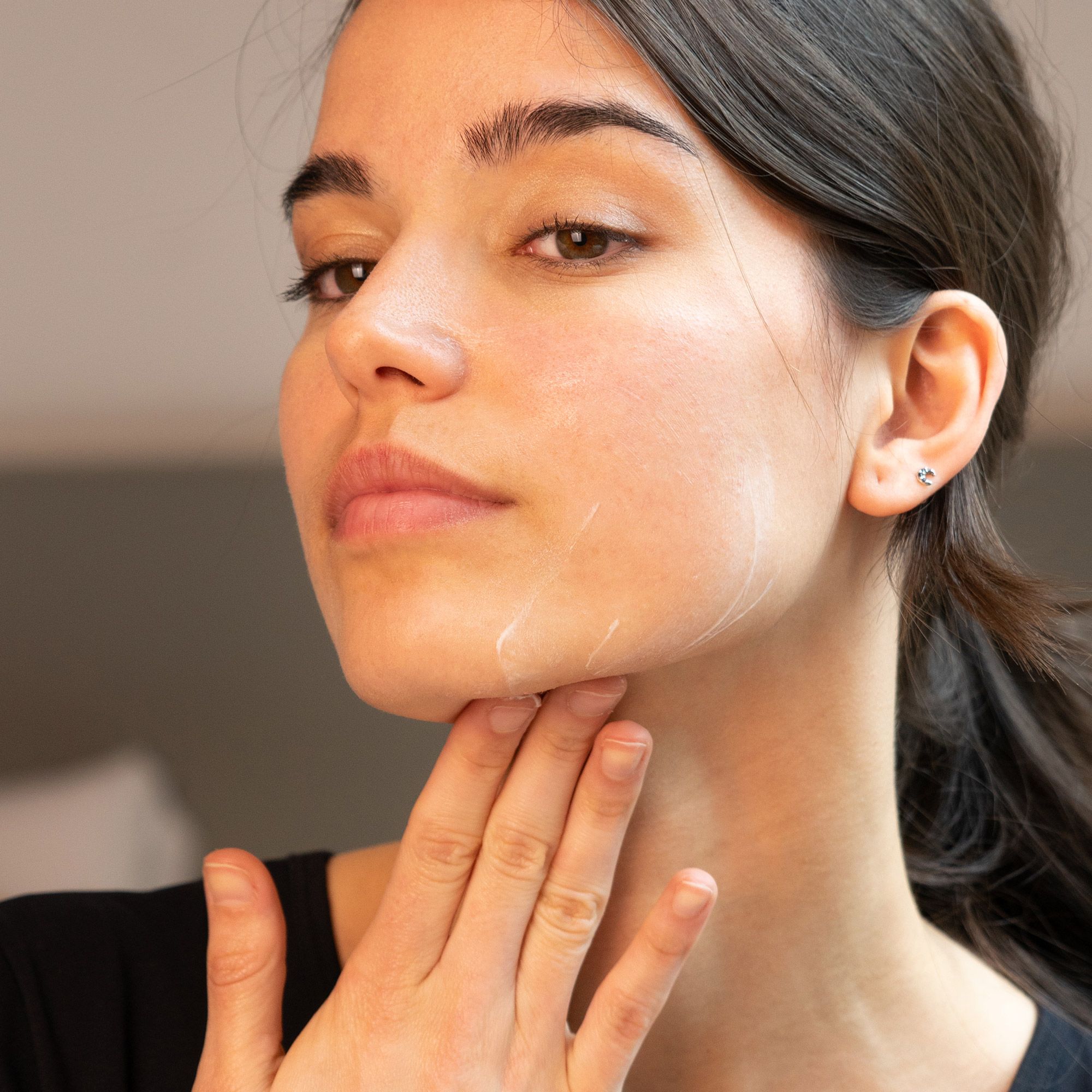Donna che si tocca il viso. Applicazione di crema. Nessuna denominazione del prodotto visibile.