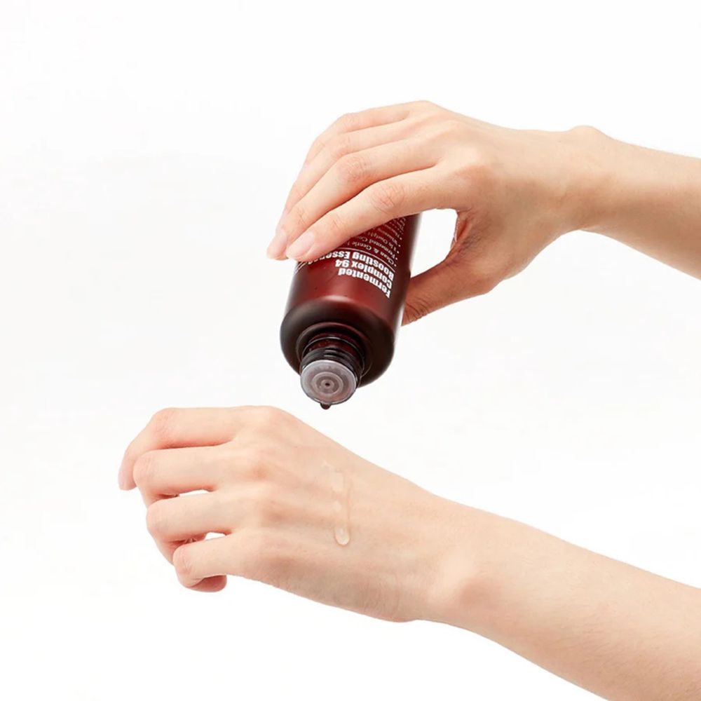 Mani che tengono un flacone marrone. Liquido che gocciola sul palmo. Prodotto: Fermented Complex 94 Boosting Essence.