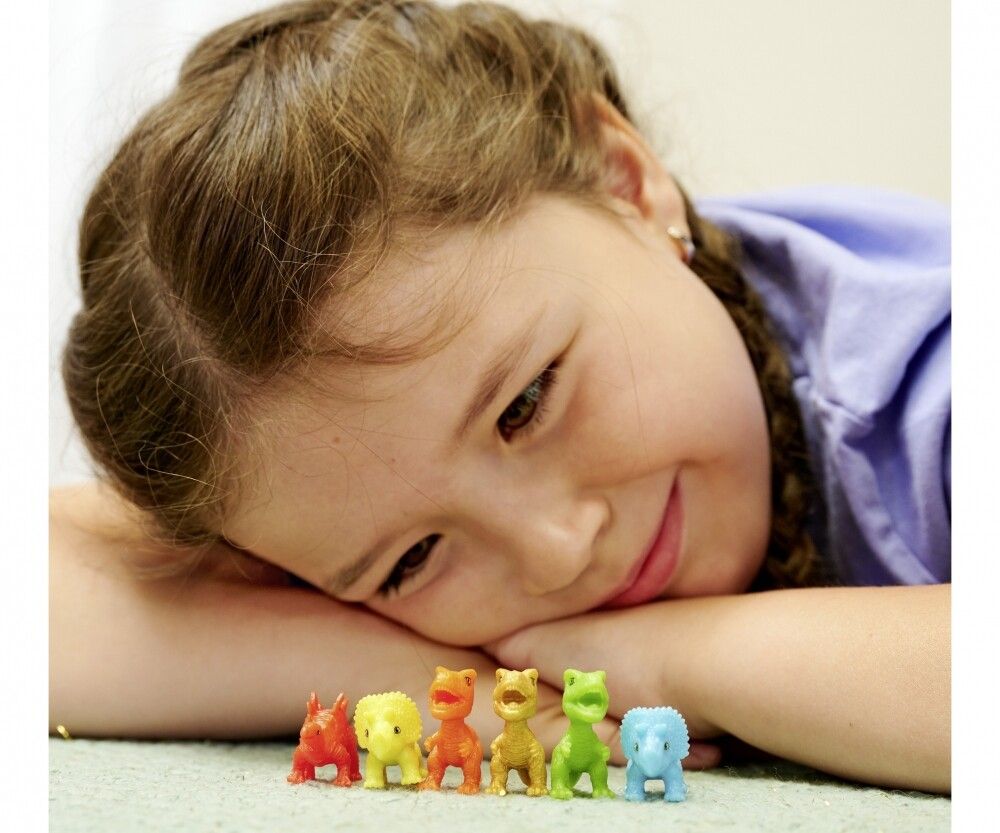 Sei piccole figure di dinosauri colorati. Bambina sdraiata a pancia in giù.