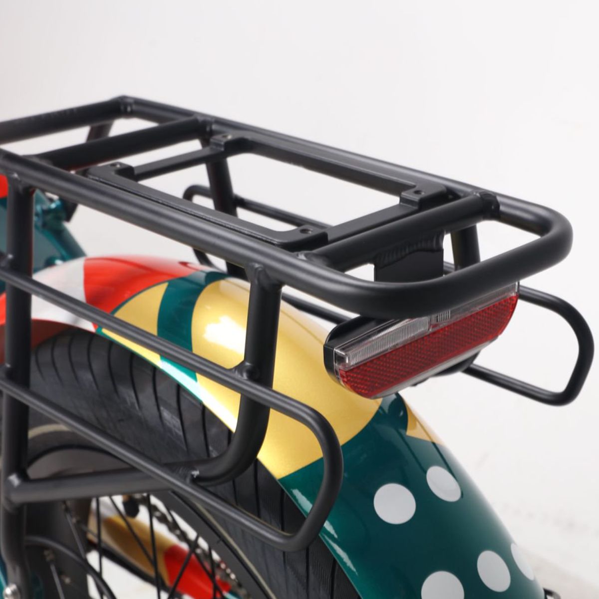 Portapacchi e fanale posteriore di una e-bike. Portapacchi nero, fanale posteriore rosso. Design verde-giallo del parafango con pois bianchi.