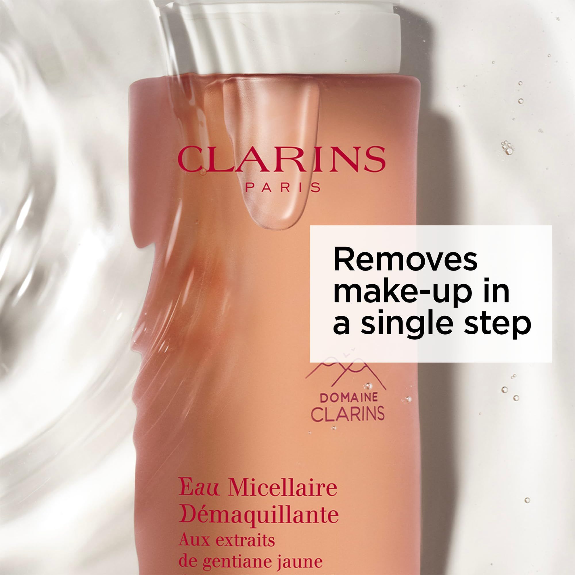 Flacone rosa, l'acqua scorre sopra. Testo: Clarins, Eau Micellaire Démaquillante. Rimuove il trucco in un solo passaggio.