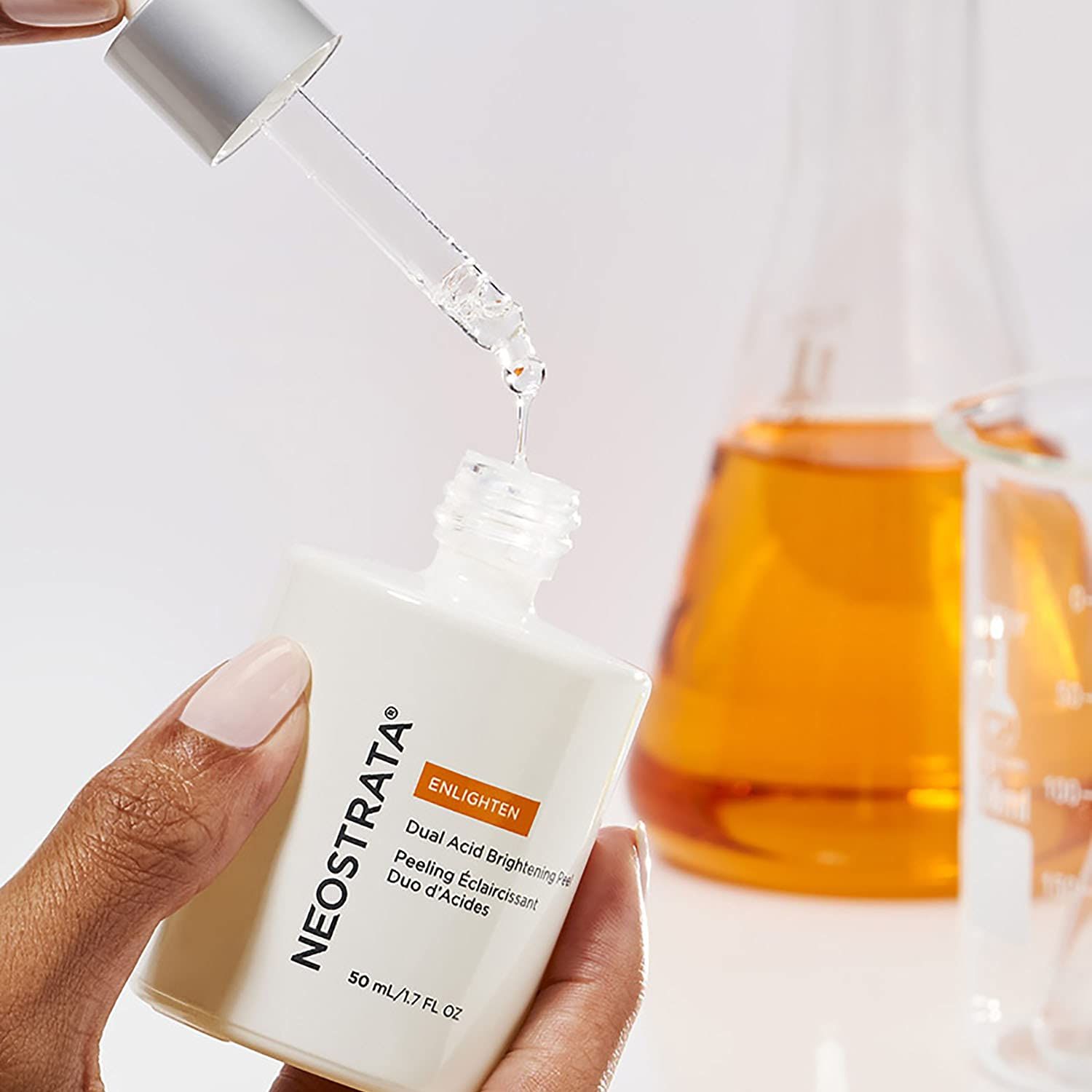 Flacone bianco con pipetta, liquido che gocciola. Testo: "NEOSTRATA", "ENLIGHTEN", "50 ml". Sfondo: attrezzature di laboratorio.