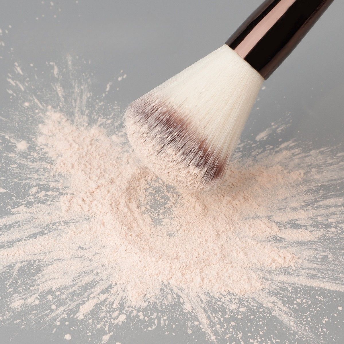 Un pennello da trucco con setole bianche e manico scuro, immerso in una cipria rosa pallido.