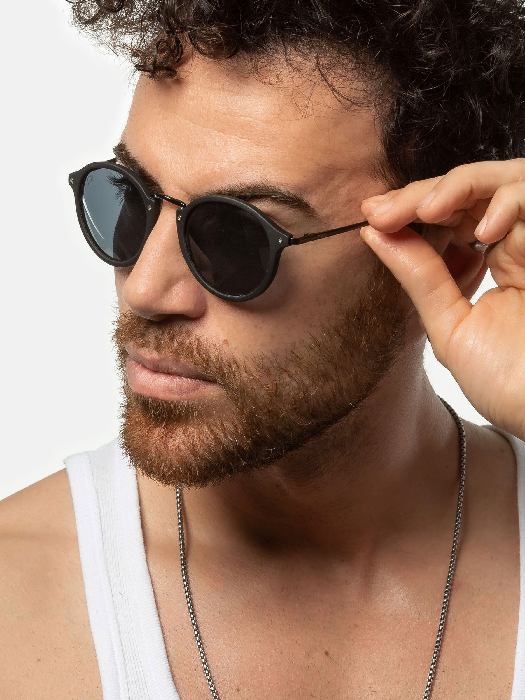 Uomo con occhiali da sole. Lenti rotonde nere, montatura nera. Indossa una canotta.