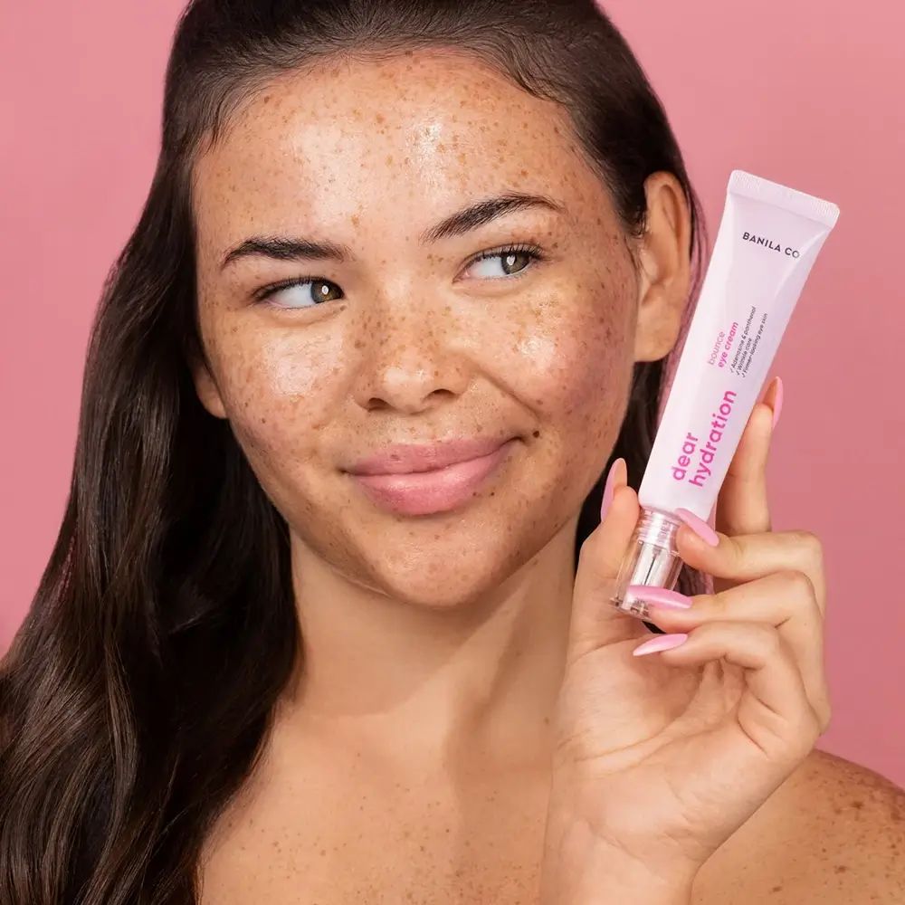 Donna tiene in mano un tubetto rosa di crema per gli occhi. Sul tubetto c'è scritto "BANILA CO Dear Hydration".
