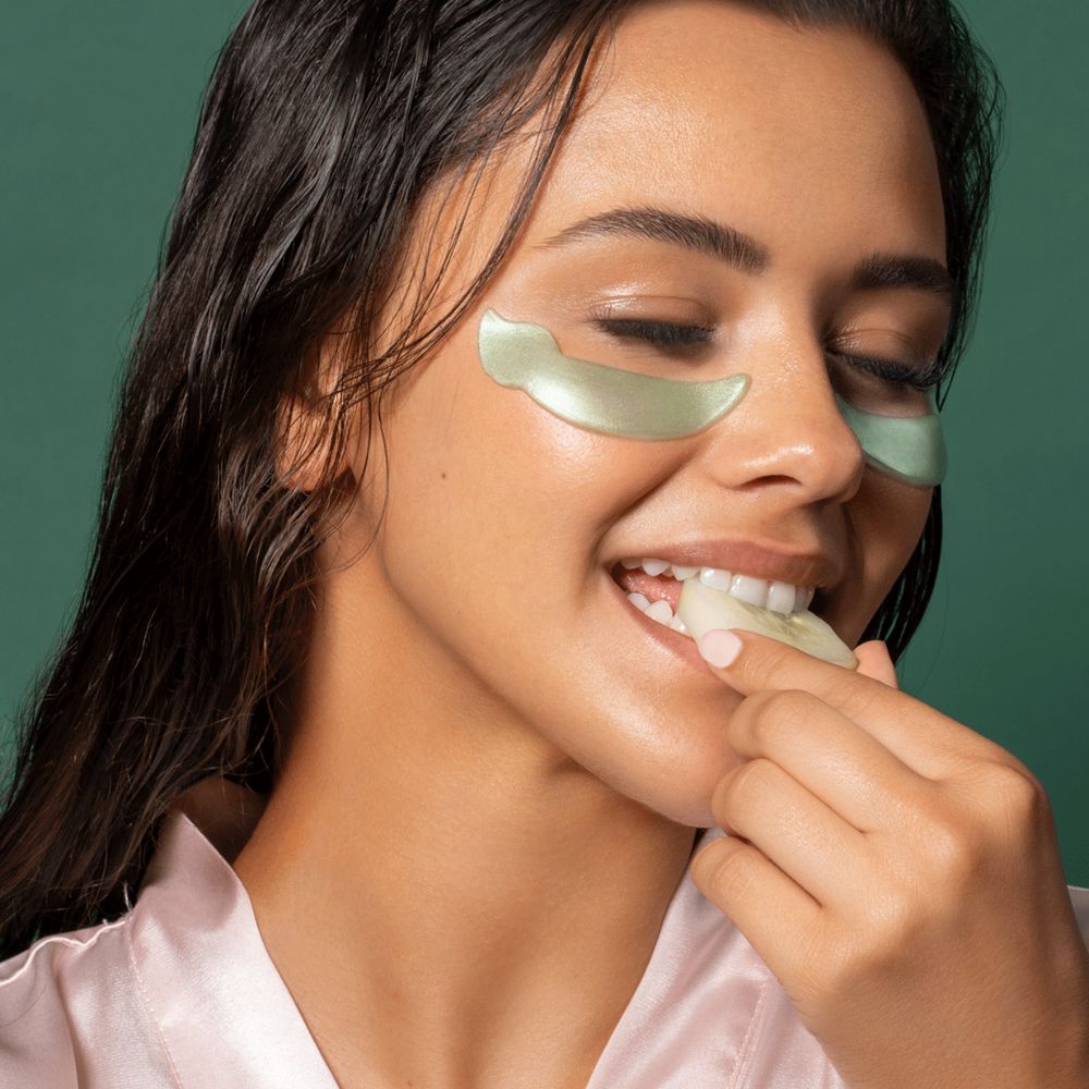 Donna con patch per gli occhi, che mette un pezzo di maschera in bocca. Patch verdi.