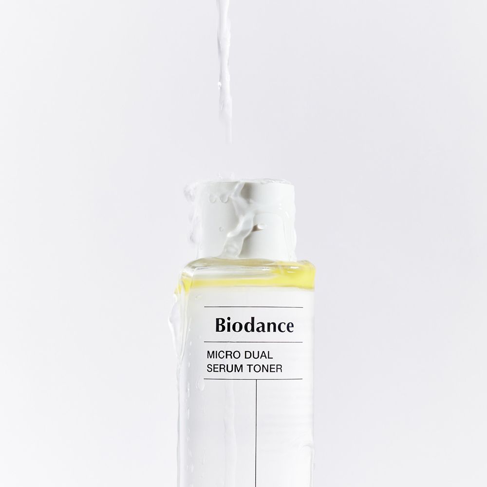 Flacone di BIODANCE Micro Dual Serum Toner. Liquido che esce dal flacone. Tappo bianco, flacone trasparente con liquido giallo.