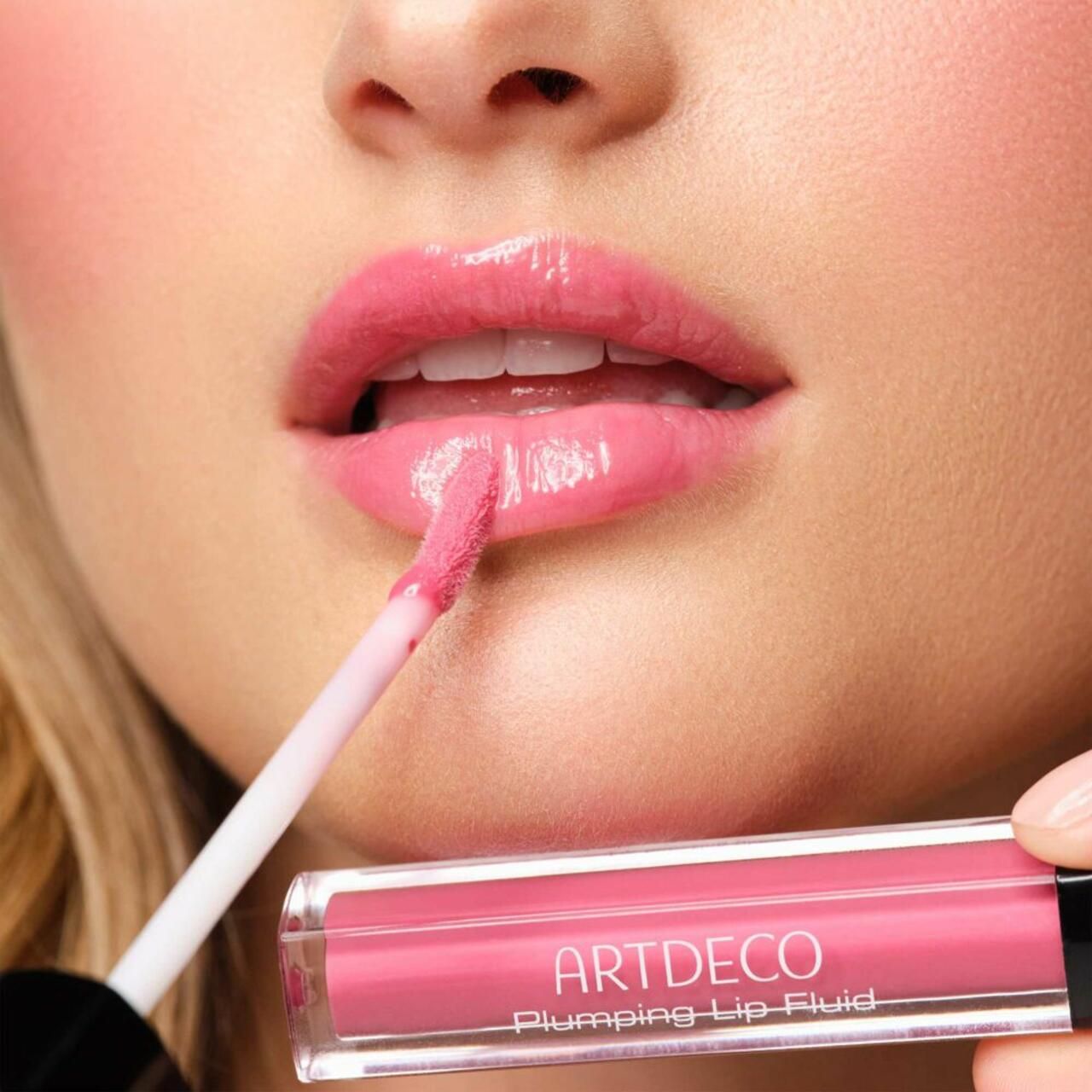 Persona che applica Artdeco Plumping Lip Fluid. Rossetto rosa applicato con applicatore. Prodotto e labbra visibili.