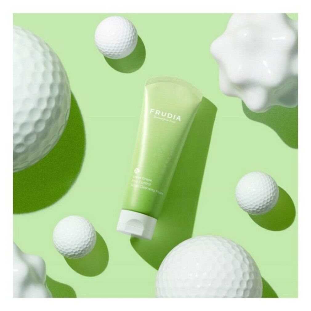 Tubo verde con tappo bianco. Scritta: FRUDIA. Testo: Green Grape Pore Control Scrub Cleansing Foam. Circondato da oggetti bianchi.