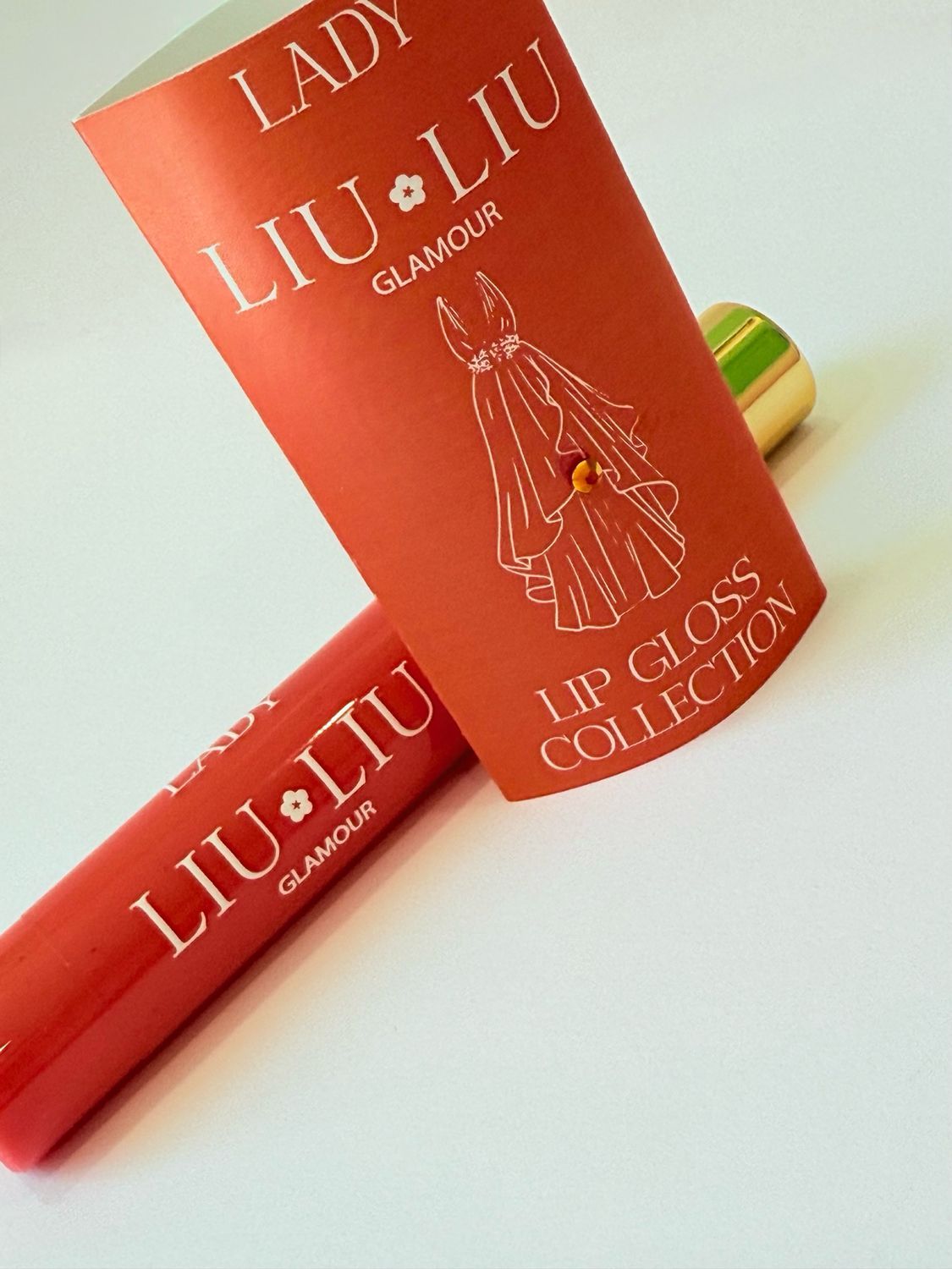 Rossetto rosso e confezione arancione. Scritta "LADY LIU LIU GLAMOUR" e disegno di un vestito.