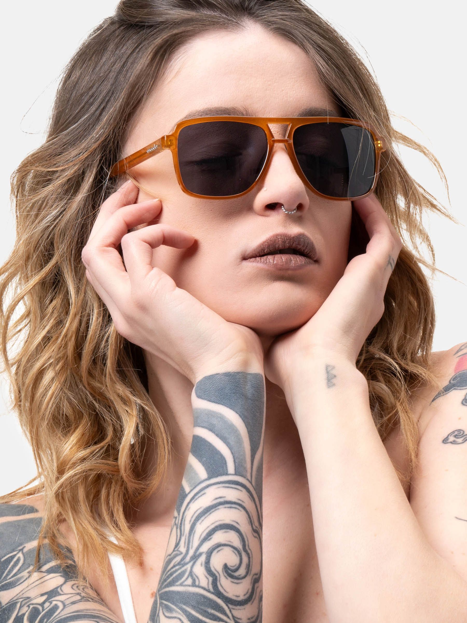 Persona con occhiali da sole con montatura marrone e lenti scure. Mani sul viso.