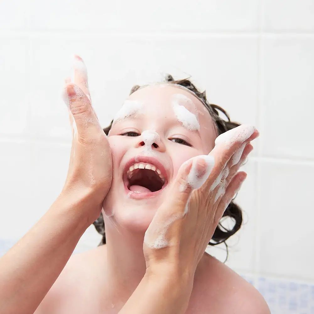 Bambino con schiuma sul viso, mani che toccano il viso. Il bambino ride.
