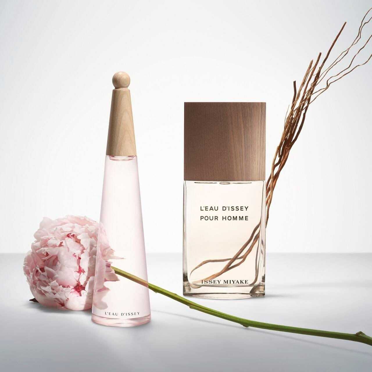 Due flaconi e un fiore. Flacone rettangolare con tappo in legno. Scritta: L'EAU D'ISSEY POUR HOMME e ISSEY MIYAKE.