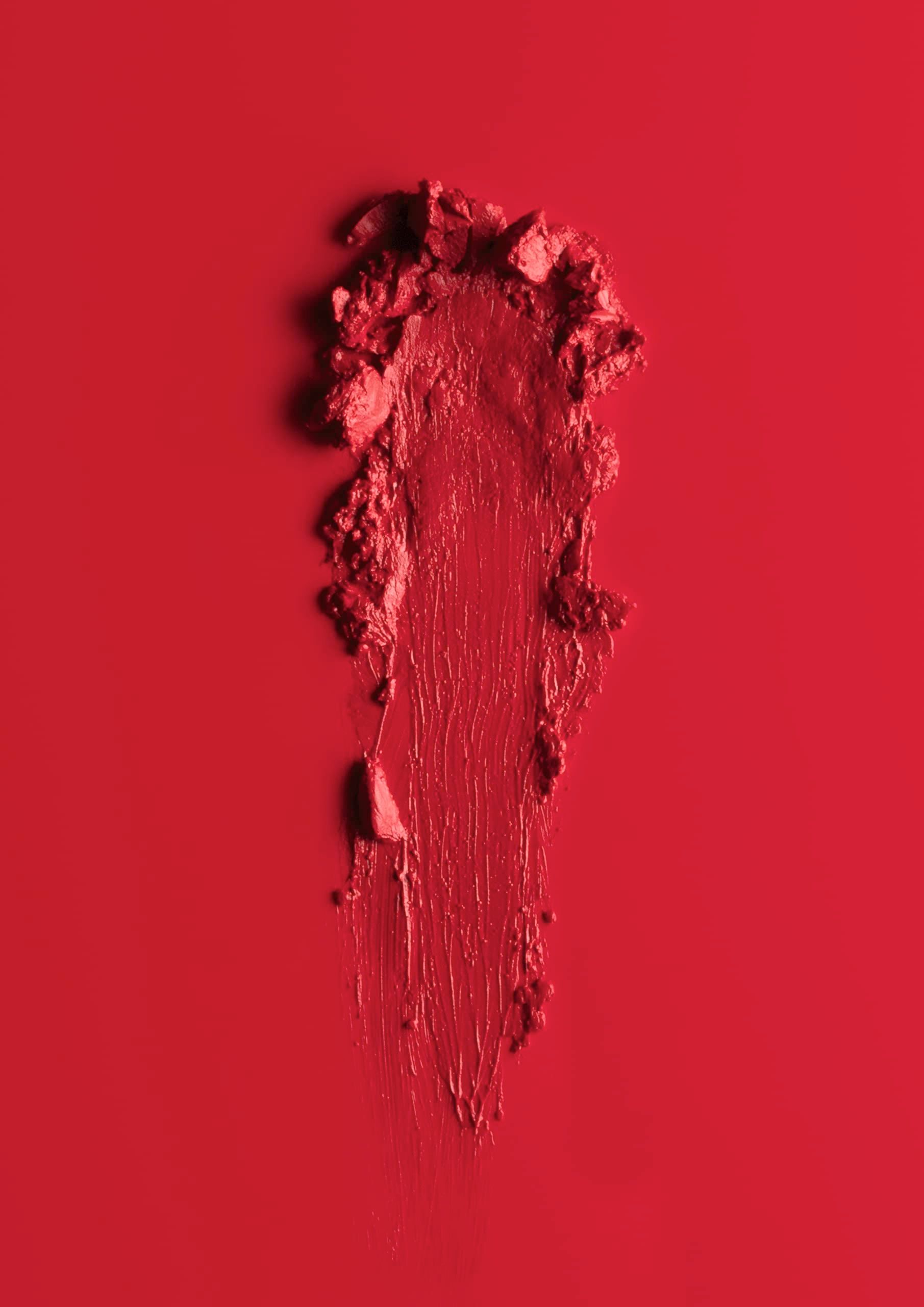 Traccia di rossetto rosso su sfondo rosso. Texture con particelle visibili.