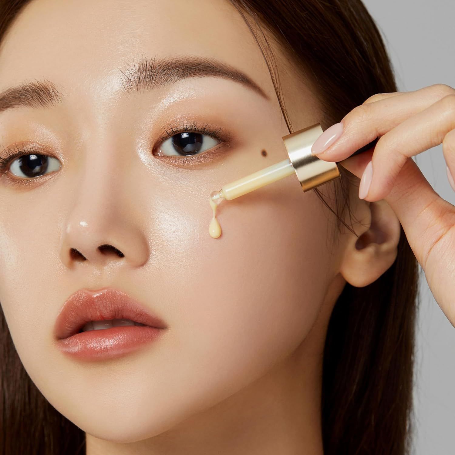 Primo piano di una donna che applica il siero sul viso con una pipetta. La pelle è lucida. Pipetta dorata.