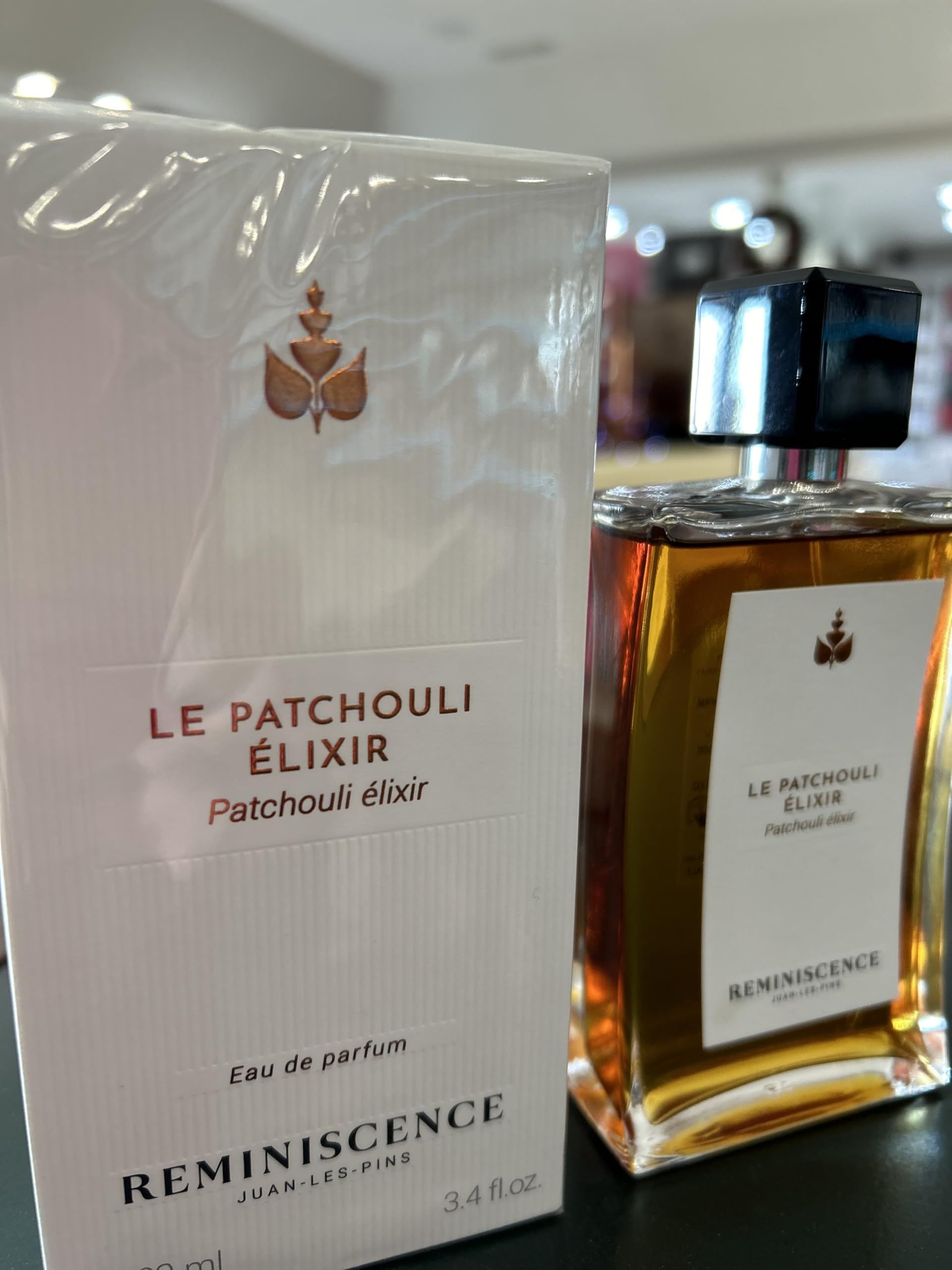 Flacone di profumo e confezione. Flacone con liquido dorato, etichetta bianca. Confezione bianca con logo e testo.