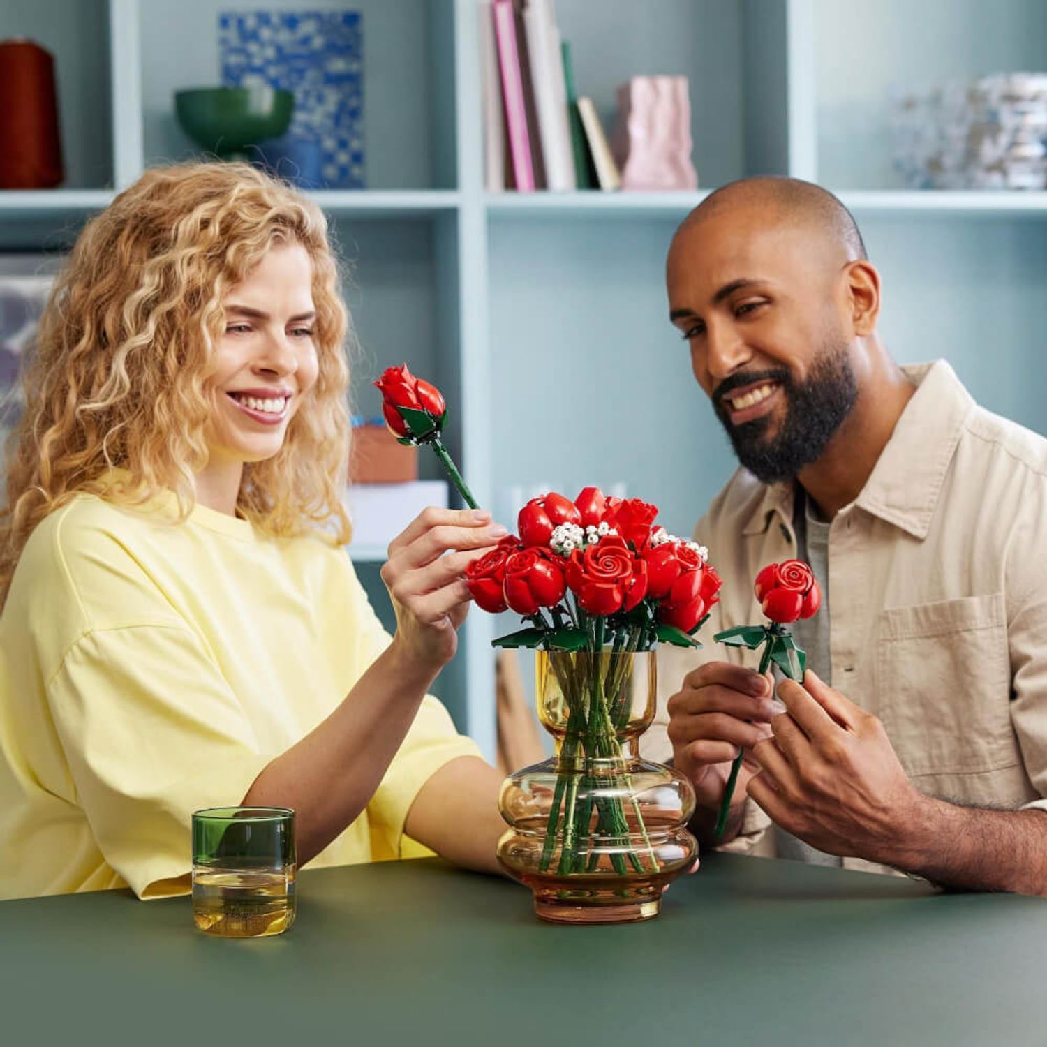 Una coppia guarda un bouquet di rose in un vaso. Una persona tiene una rosa.