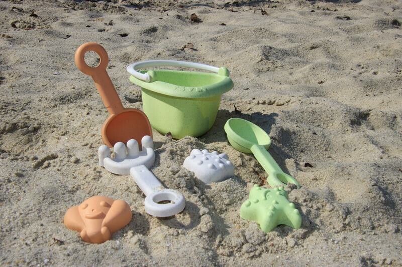 Secchiello verde, paletta arancione, rastrello verde, cucchiaio beige e formine sulla sabbia. Giocattoli per bambini.