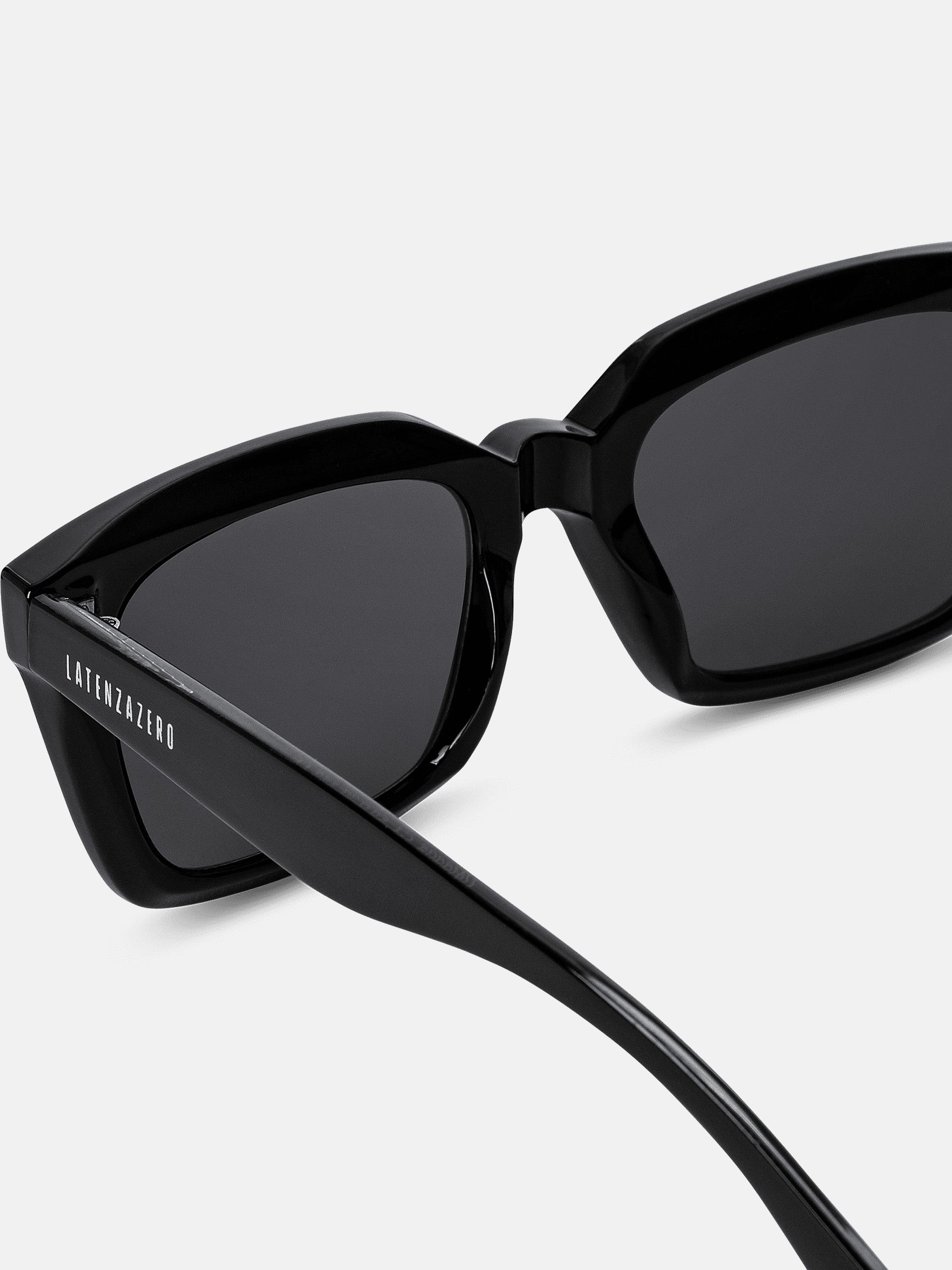 Primo piano di occhiali da sole neri. Lenti rettangolari, montatura nera. Marchio sulla stanghetta. Materiale lucido.