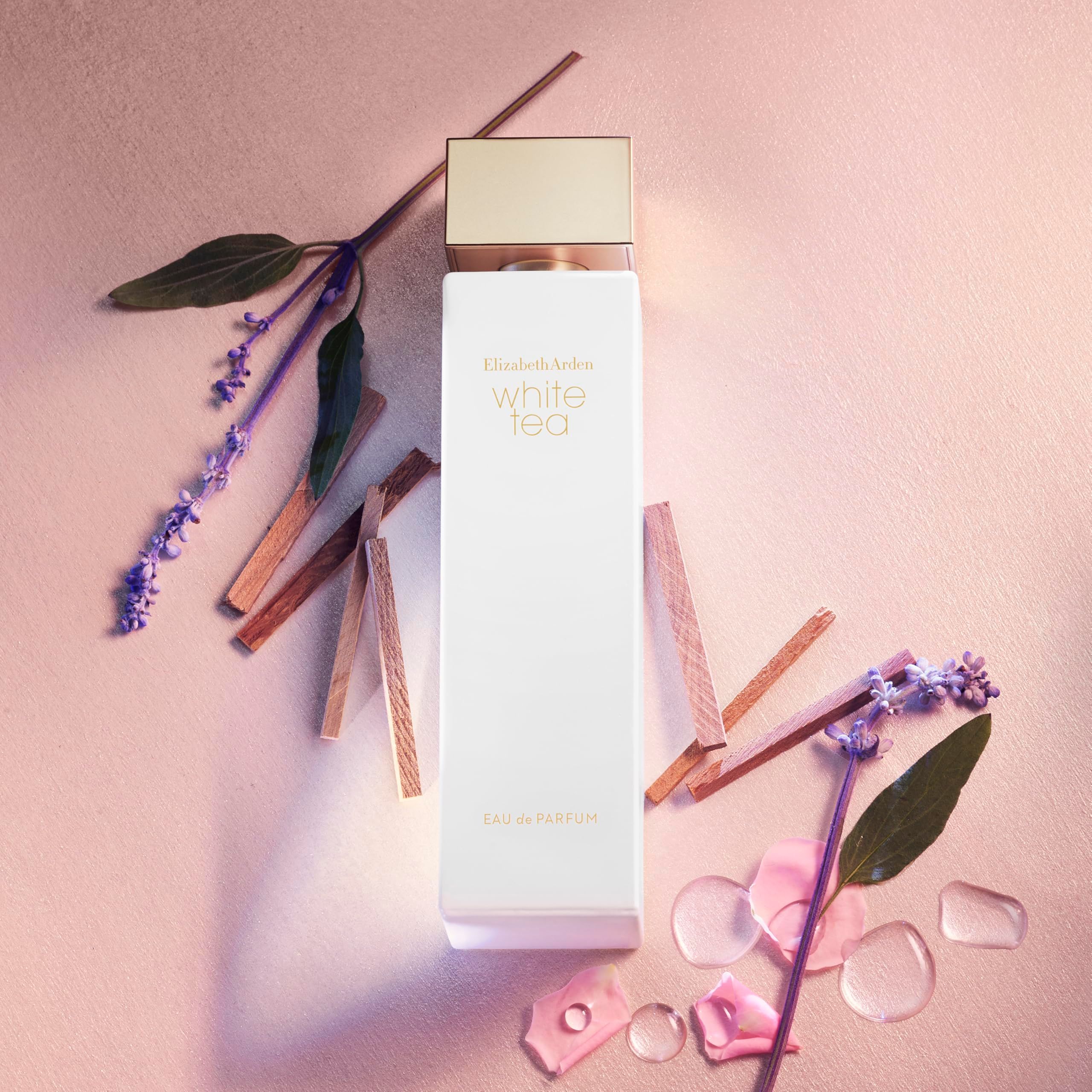 Flacone di profumo bianco, tappo dorato. Scritta: White Tea, Elizabeth Arden. Decorato con fiori e rami.