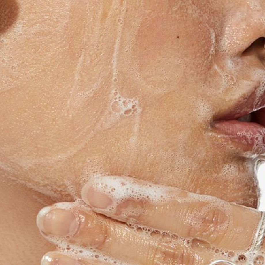Primo piano di una persona che si lava il viso con un gel schiumoso. Nome del prodotto non incluso.