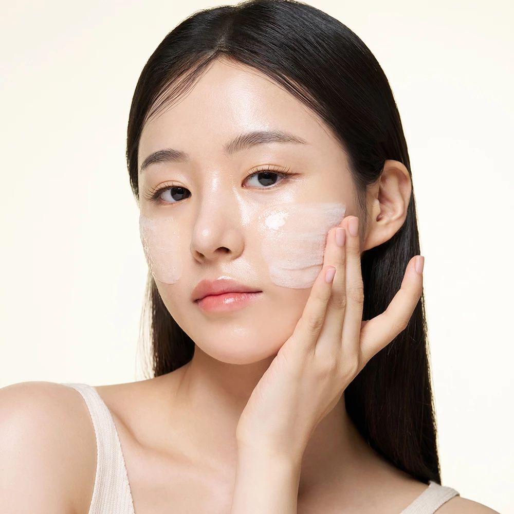 Una donna indossa un top bianco. Applica una sostanza trasparente sul viso.