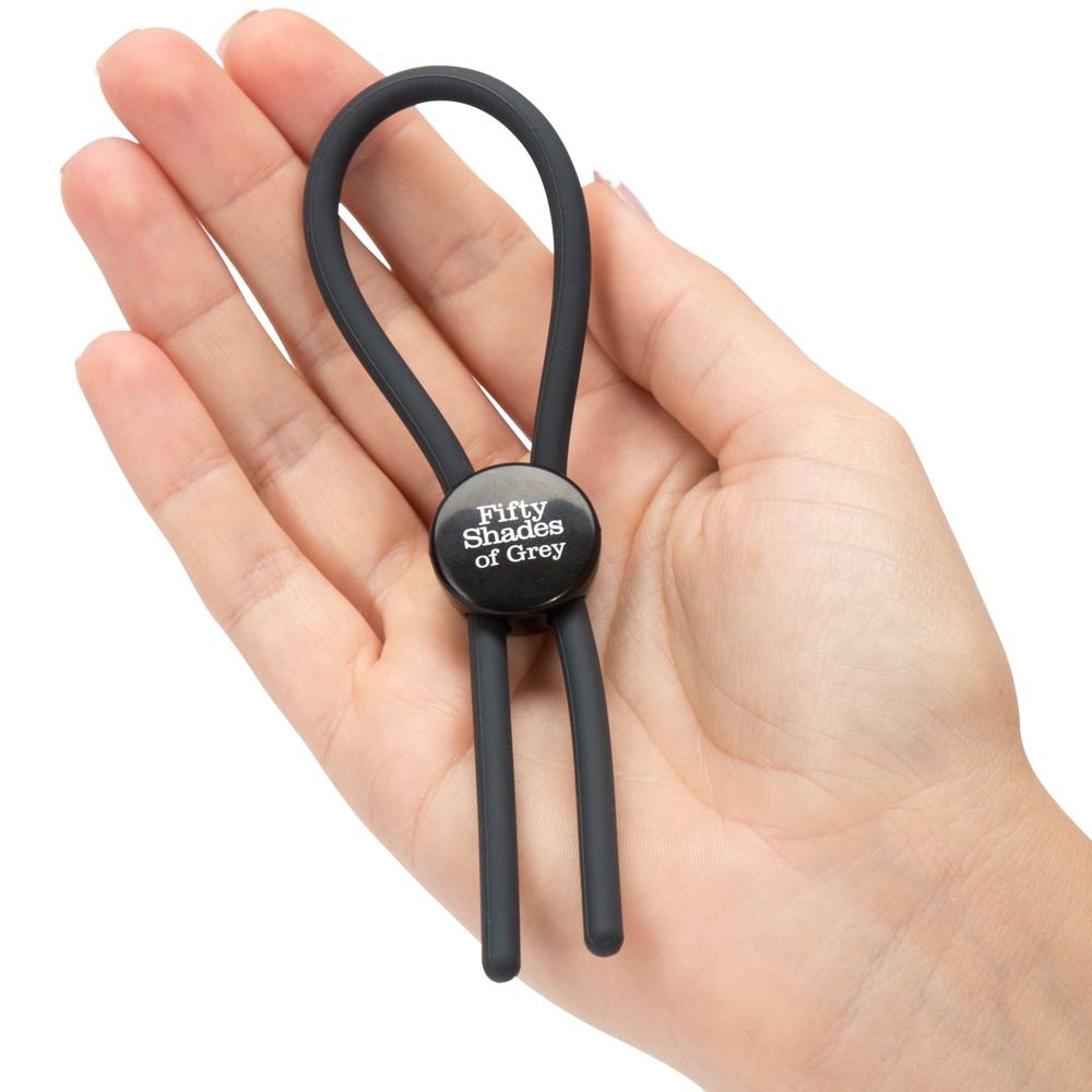 Anello fallico nero con logo Fifty Shades of Grey, posto attorno a un pene. Due fili scendono.