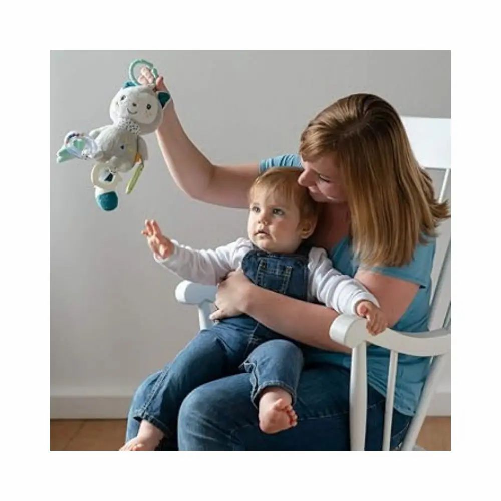Madre tiene in braccio un bambino. Il bambino afferra un peluche grigio con orecchie blu, stella, specchio e sonaglio.