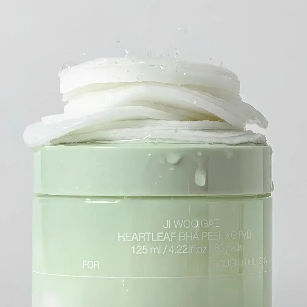 Contenitore verde con dischetti bianchi. Scritta: Heartleaf BHA Peeling Pad. Dischetti impilati, alcuni con schizzi.