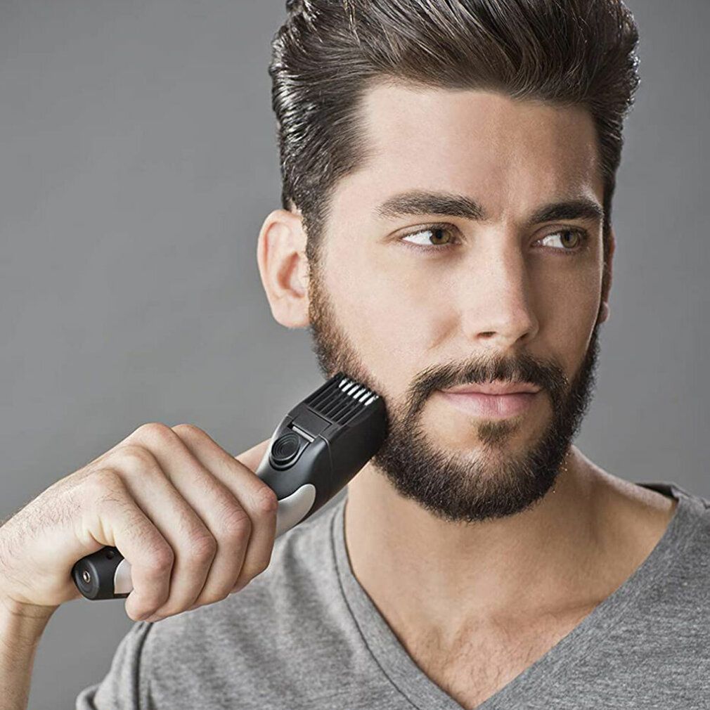 Uomo che si rade la barba con un tagliabarba. Dispositivo nero e argento. La barba viene tagliata.