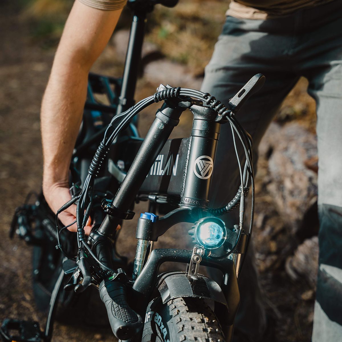 Primo piano del manubrio di una e-bike Vitilan V3 2.0. Faro, logo e dettagli visibili. Persona che tiene la bici.