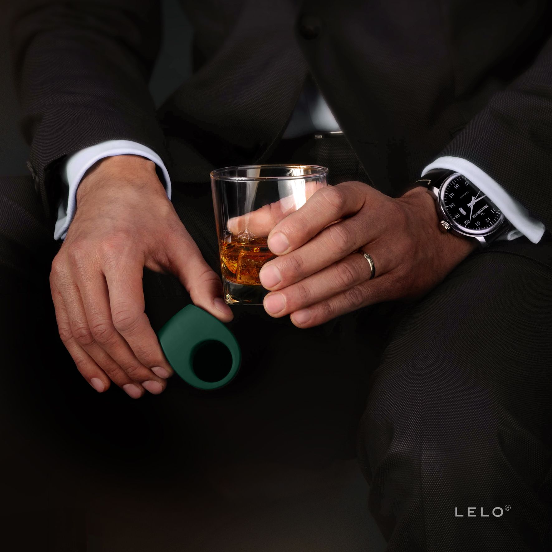 Uomo che tiene un anello vibrante verde scuro e un bicchiere di whisky.