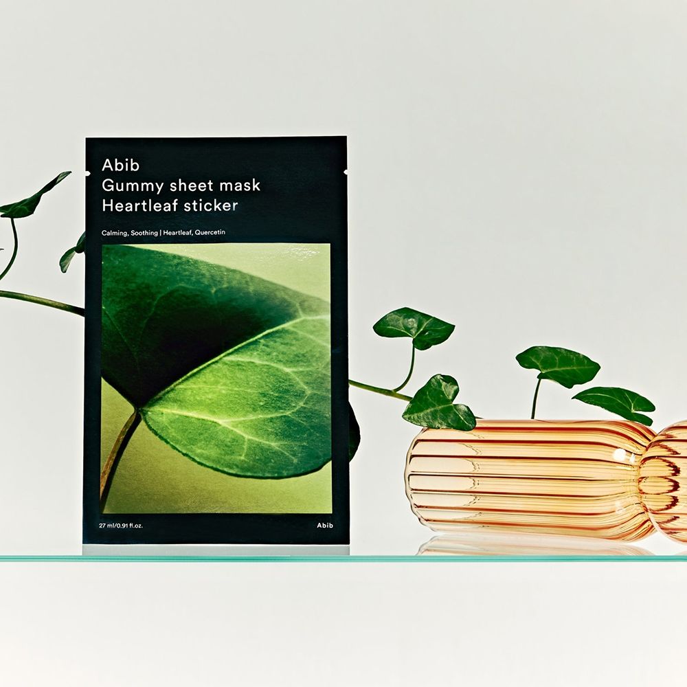 Confezione del prodotto con motivo a foglia e testo: ABIB Gummy Sheet Mask Heartleaf sticker. Decorazione con piante e vetro.