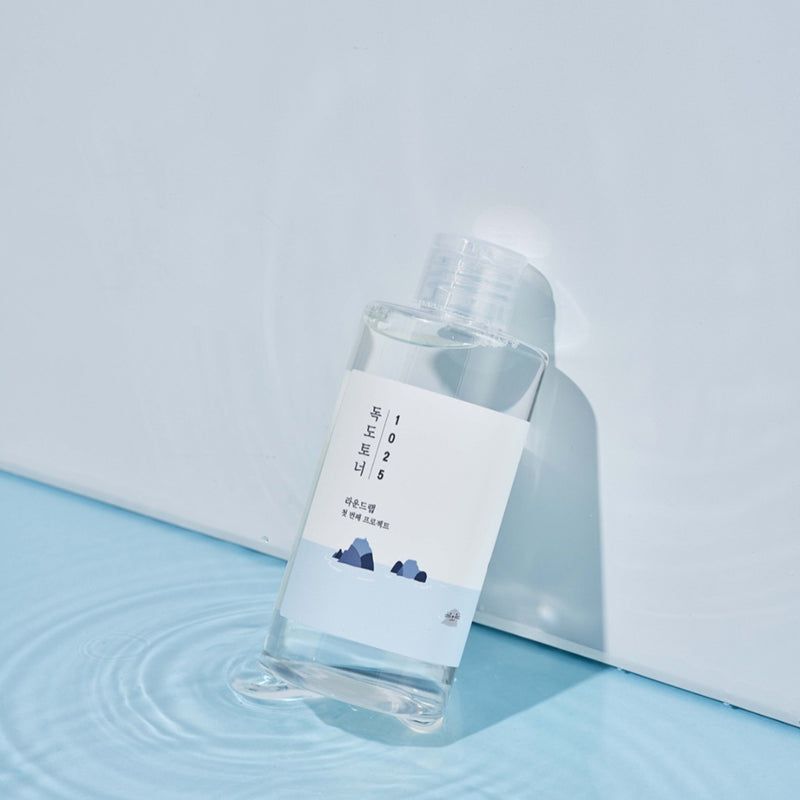 Bottiglia di liquido trasparente, etichetta bianca e testo coreano. Su sfondo blu. Gioco di ombre.