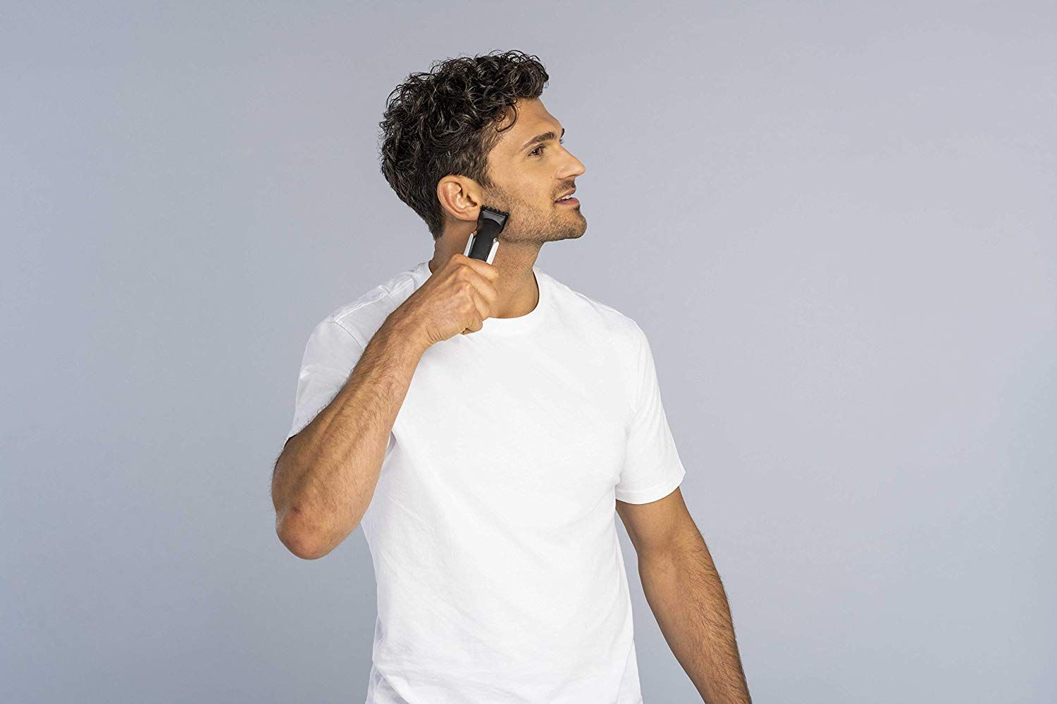 Uomo che si rade con un tagliacapelli. L'uomo indossa una maglietta bianca. Il dispositivo è nero, argento e bianco.