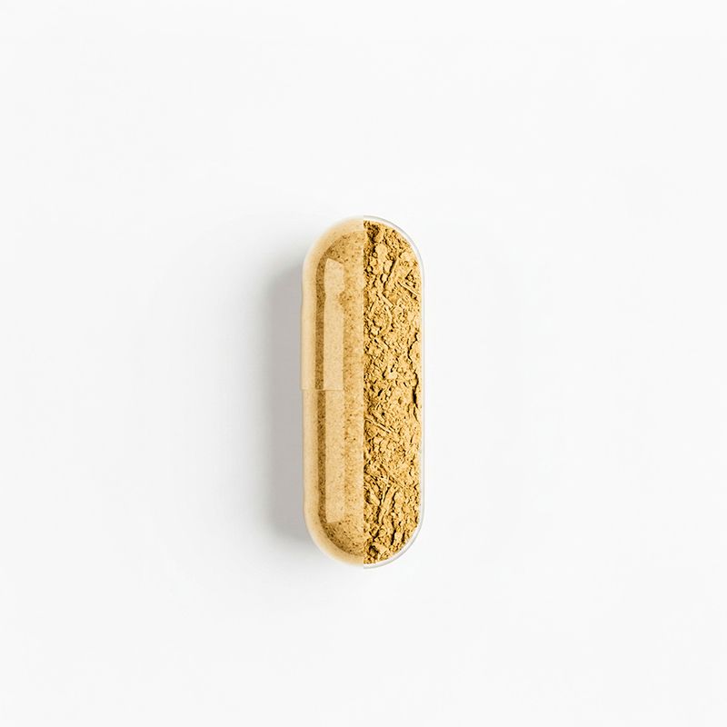 Una singola capsula riempita di polvere beige, su sfondo bianco.