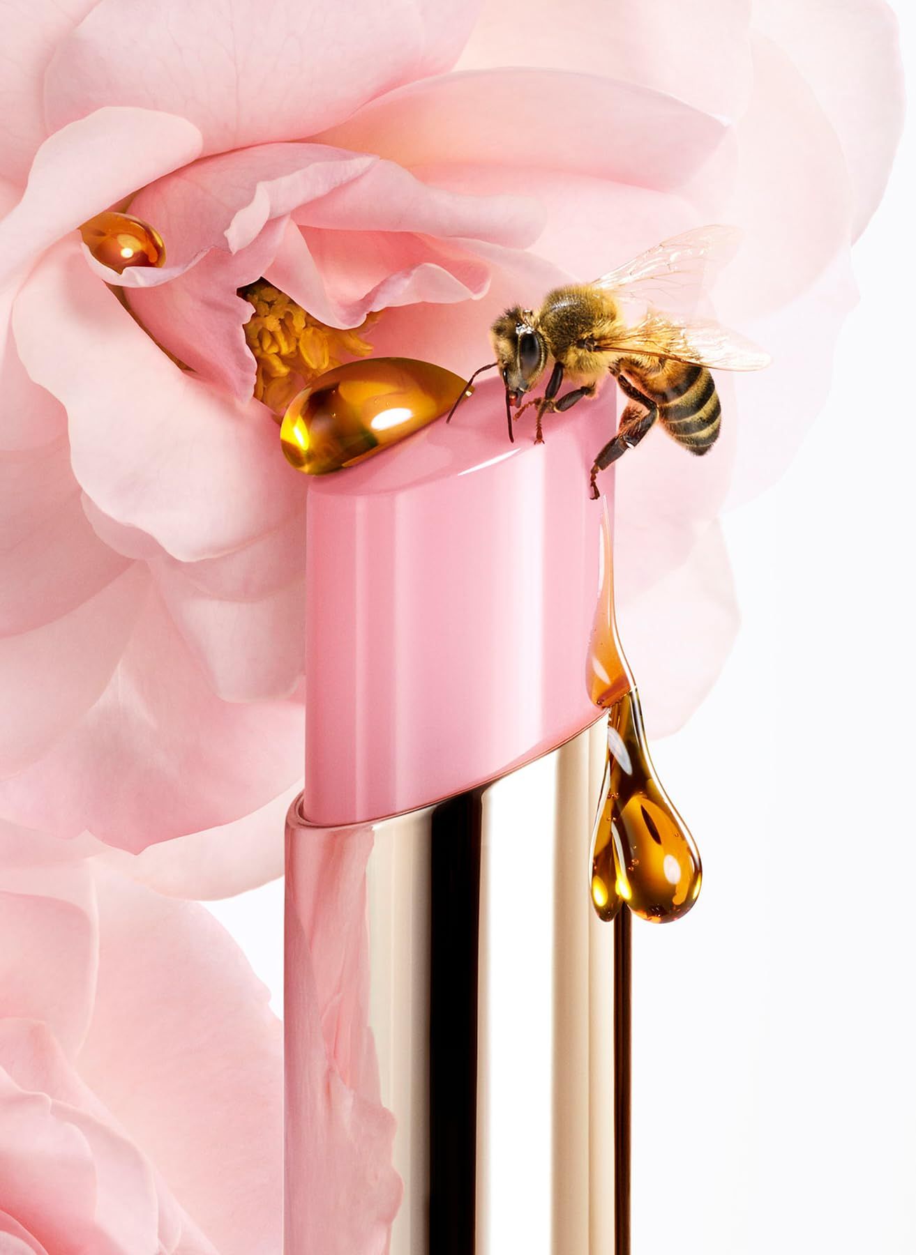Un balsamo per labbra rosa con custodia dorata, con un'ape e gocce di miele su un fiore rosa.
