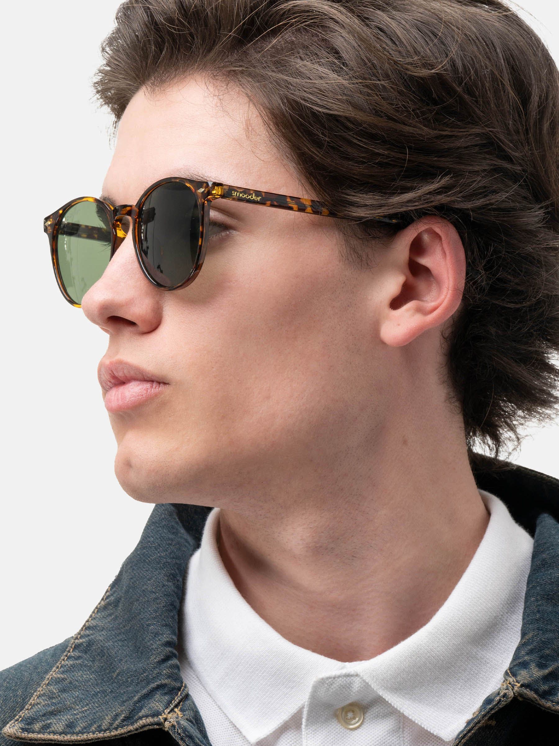 Uomo con occhiali da sole marroni tartarugati, lenti verdi. Logo del marchio sulla stanghetta.