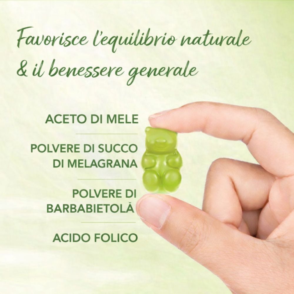 Mano che tiene un orsetto gommoso verde. Testo: Aceto di mele, Polvere di succo di melograno, Polvere di barbabietola, Acido folico.