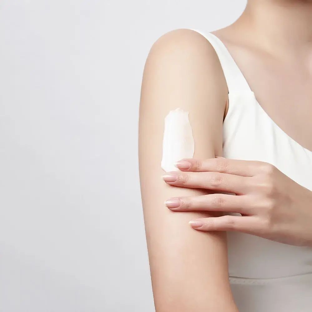 Braccio con crema bianca applicata. La persona indossa una canotta bianca.
