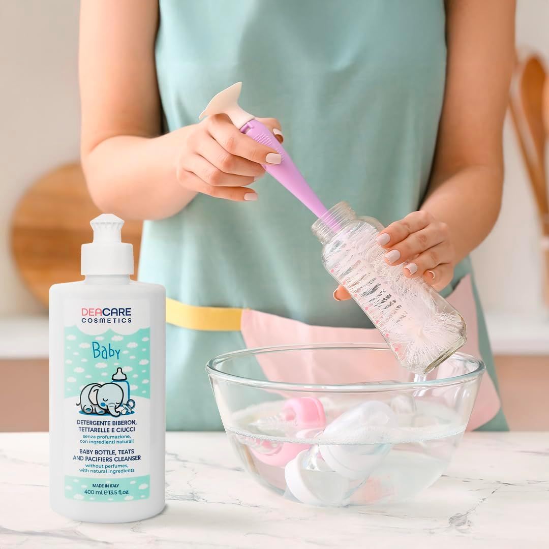 Una persona pulisce un biberon con uno scovolino. Accanto, una bottiglia di DEACARE Baby Detergente.