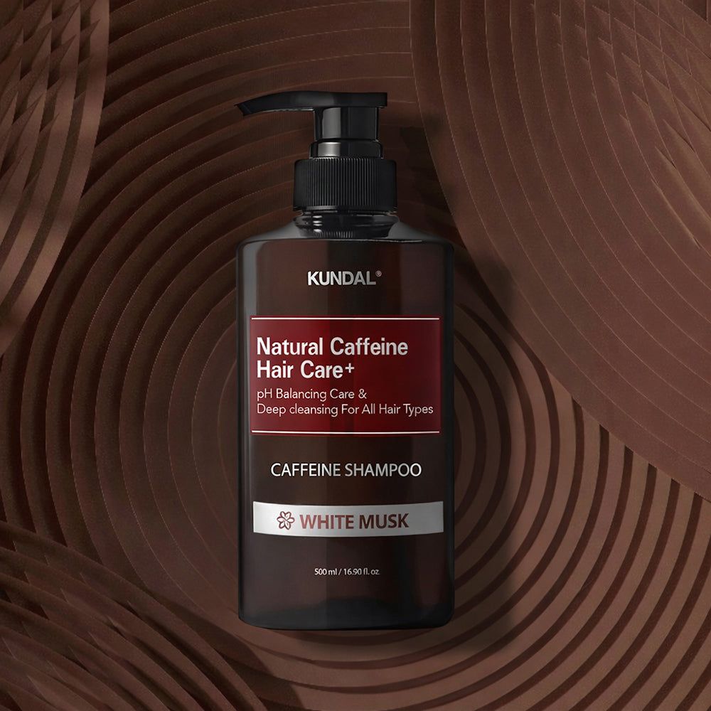 KUNDAL Natural Caffeine Hair Care+ Shampoo (White Musk) su sfondo decorativo marrone.