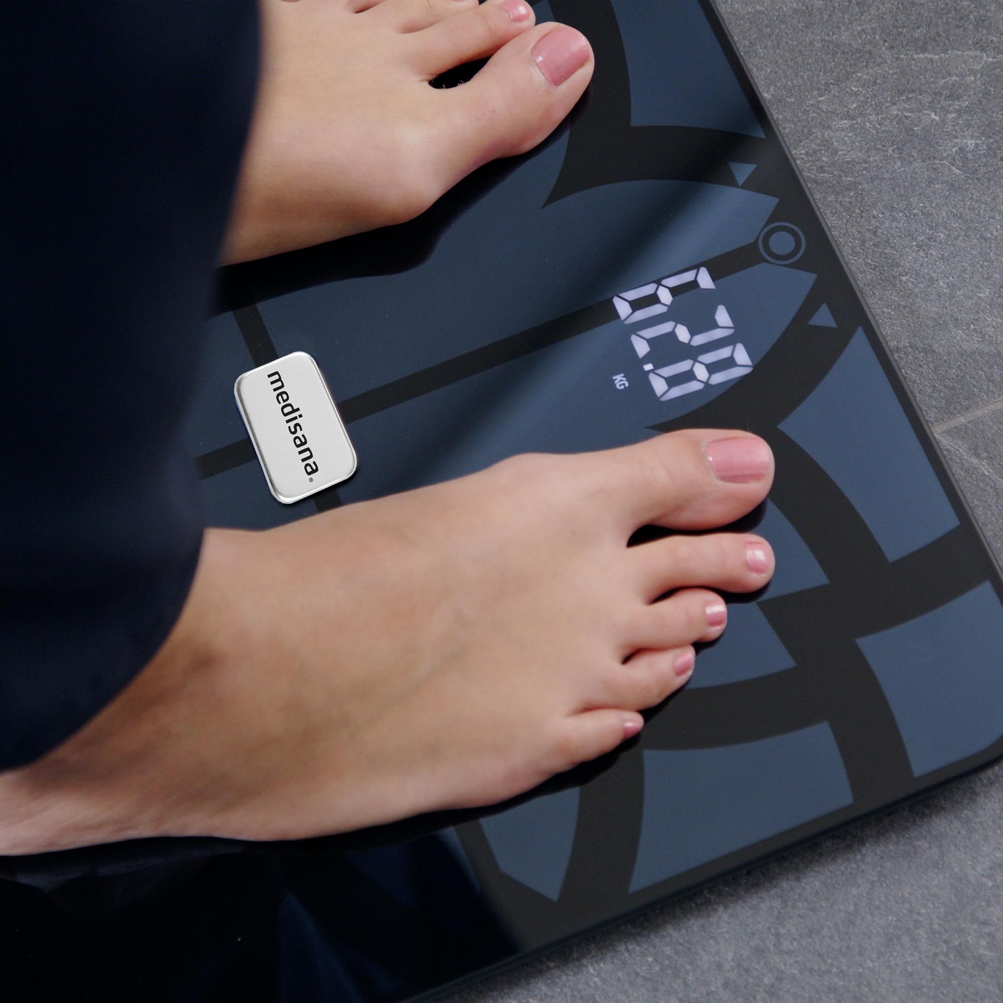 Persona in piedi su una bilancia per l'analisi corporea nera. Piedi sulla bilancia, display digitale. Marchio: medisana.