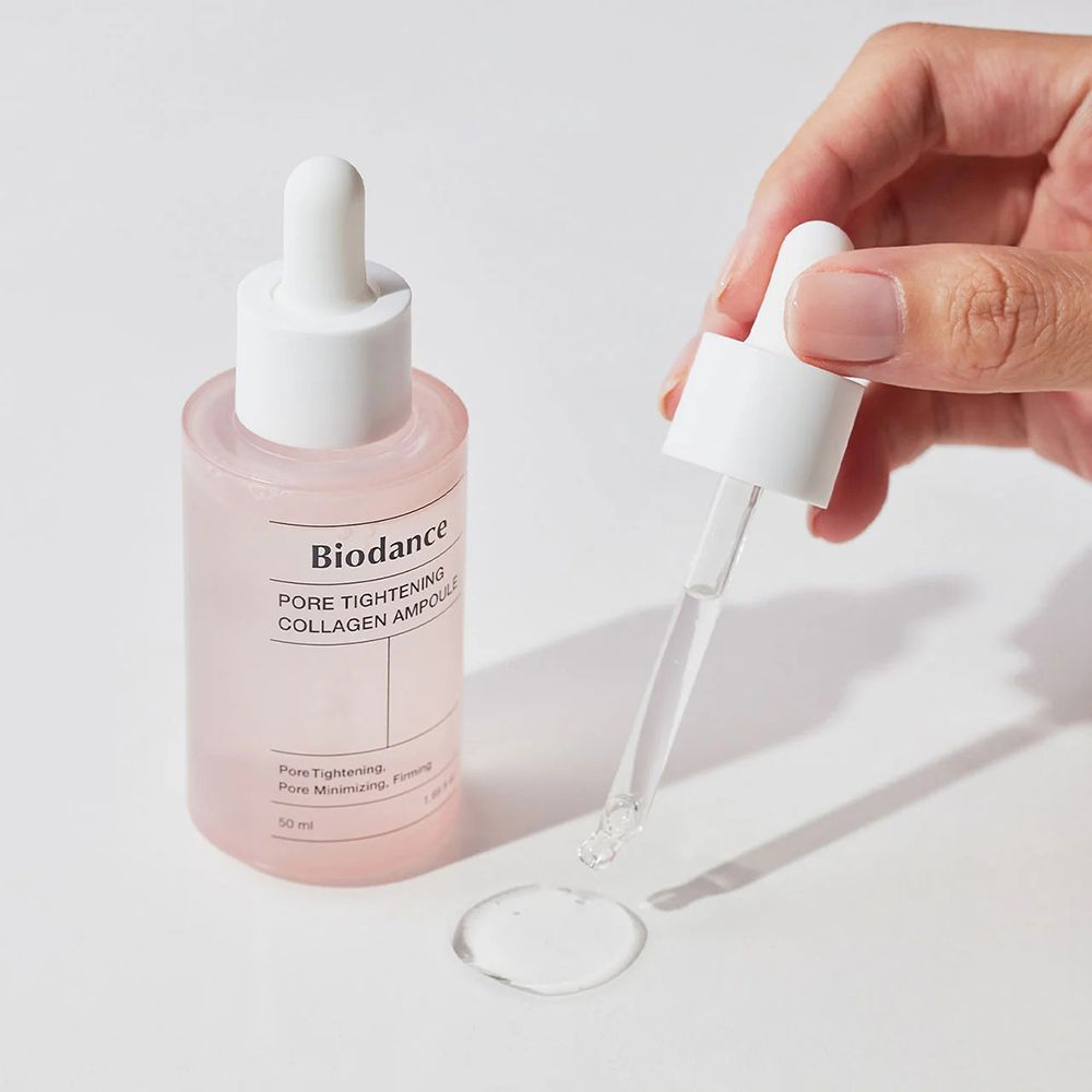 Mano che tiene un flacone rosa con tappo bianco. Scritta: Biodance PORE TIGHTENING COLLAGEN AMPOULE. Gocce.