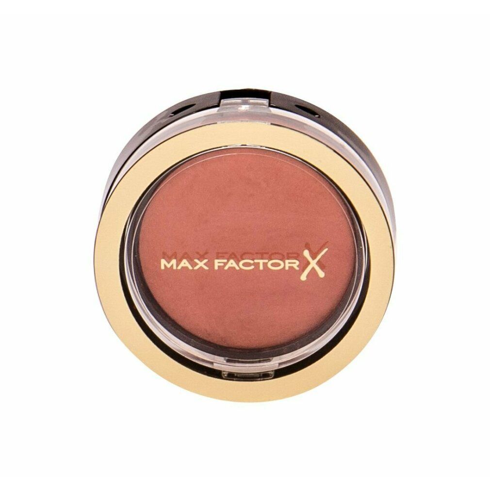 Contenitore rotondo dorato con polvere rosa. Anello nero e coperchio trasparente. Scritta: MAX FACTOR.