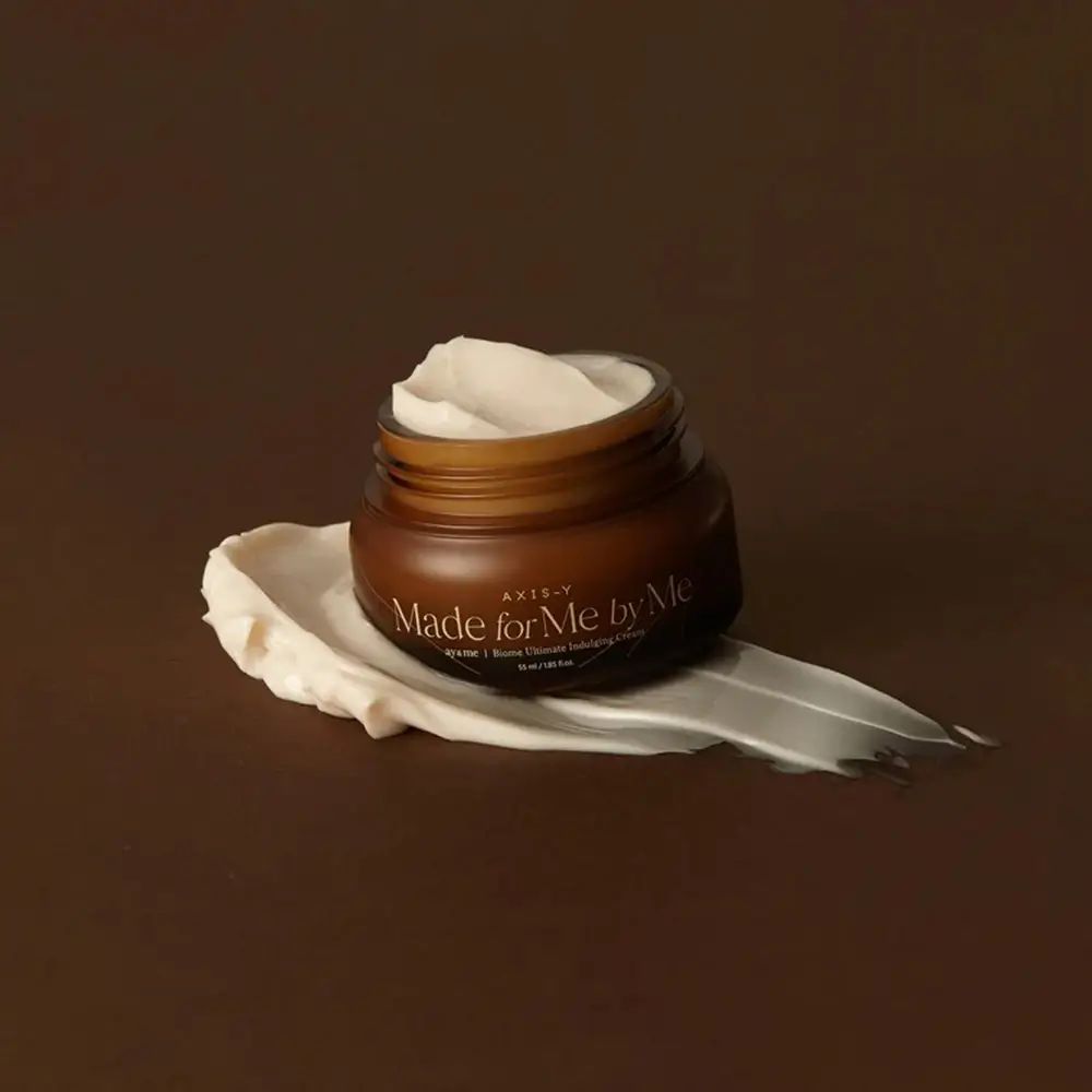 Vaso di crema in vetro marrone con crema bianca su una scia di crema. Scritta: AXIS-Y, Made for Me by Me.